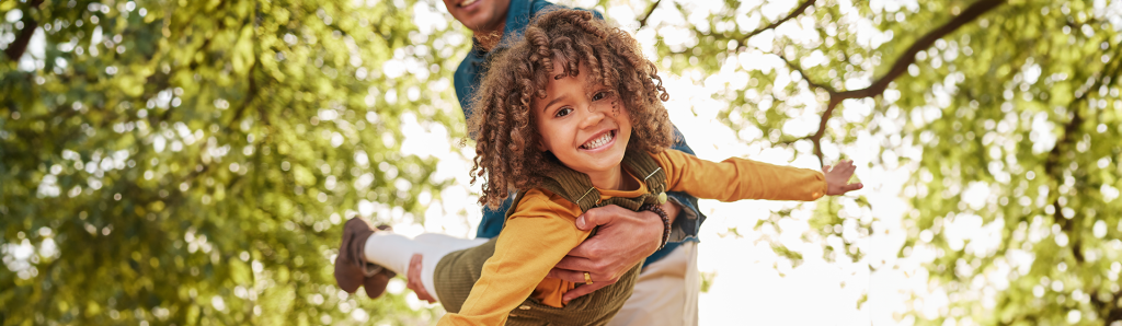 Dad swinging child like an airplane on parenting plan approved visitation in backyard by trees