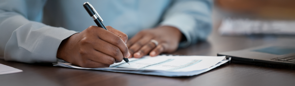 Close-up of hands signing legal documents with a black pen on a wooden desk, wearing a white dress shirt. The image conveys the professional yet personal nature of filing legal paperwork independently.