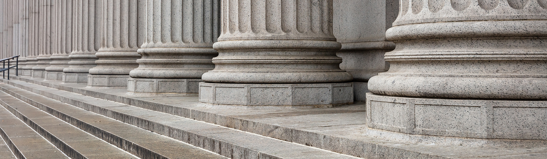 Row of classical stone columns and steps at a courthouse entrance, showing detailed architectural features in a neutral gray tone. The perspective emphasizes the ascending steps leading to the judicial building.