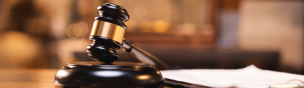 Judge's wooden gavel with brass band resting on a sound block, with court documents blurred in the background, photographed in warm lighting.