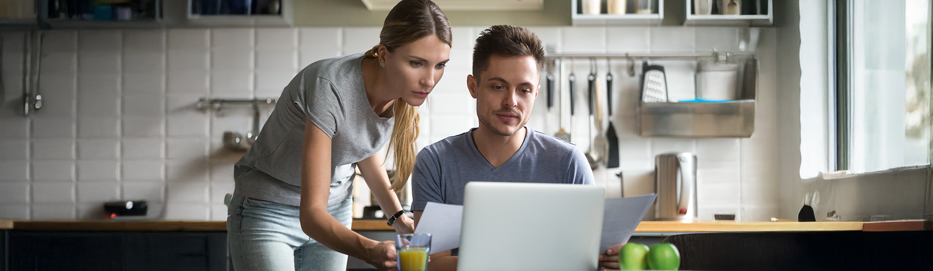 Young couple reviewing documents together at their kitchen counter while using a laptop, depicting a casual home environment for accessing online legal resources.